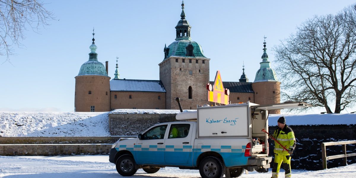 En anställd på Kalmar Energi tar fram verktyg ur en företagsbil, med Kalmar slott i vinterskrud som bakgrund. Bilden visar en del av stadens vintermiljö och företagets arbete.