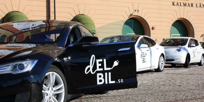 Elbilar från delbilspoolen parkerade på rad framför Kalmar läns museum, med en svart bil i förgrunden och två vita bilar i bakgrunden.