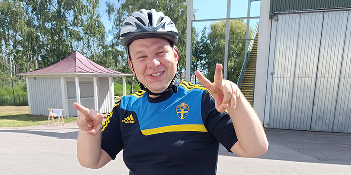 En glad kille med träningskläder och cykelhjälm som gör segertecknet.