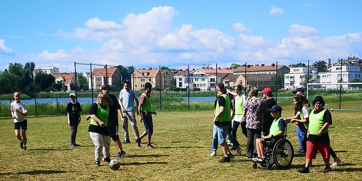 En samling barn och unga på en gräsplan utom hus som spelar fotboll.