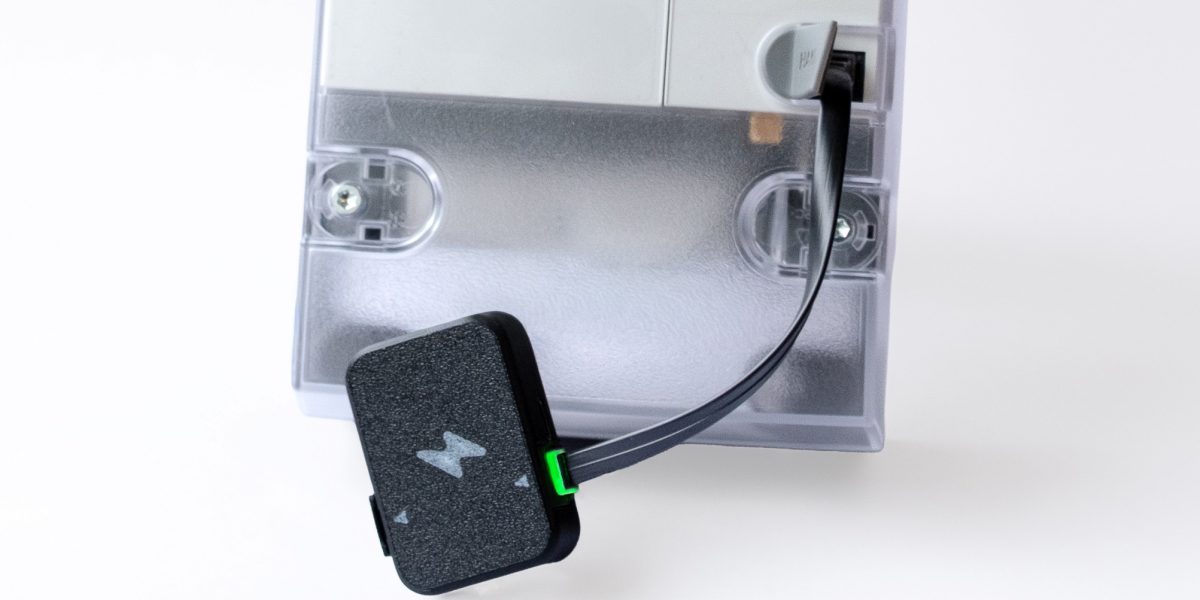 Studiobild som visar Zap realtidsmätare, med grön led, inkopplad i en elmätare med Kalmar Energis logotyp.