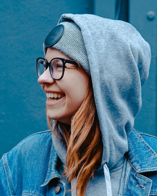 Kvinna i jeansjacka och grå huvtröja framför blå vägg.