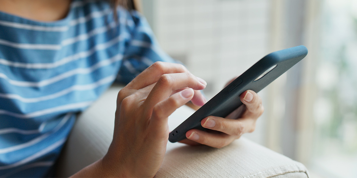 En kvinna sitter i en soffa och surfar på sin mobil.