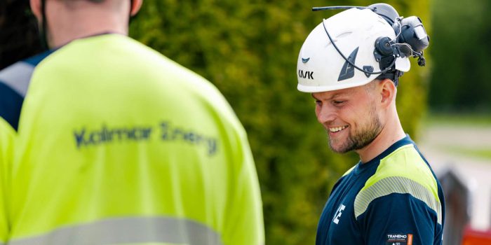 En glad medarbetare på Kalmar Energi utomhus med hjälm och varselkläder.
